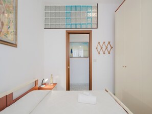 Ein Hotelzimmer mit Bett, Nachttisch, Lampe, Handtuch, Kleiderschrank, Spiegel und einer Wanddekoration.