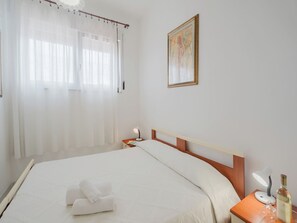 A hotel room with a bed, a nightstand with a lamp, a bottle, and a glass.