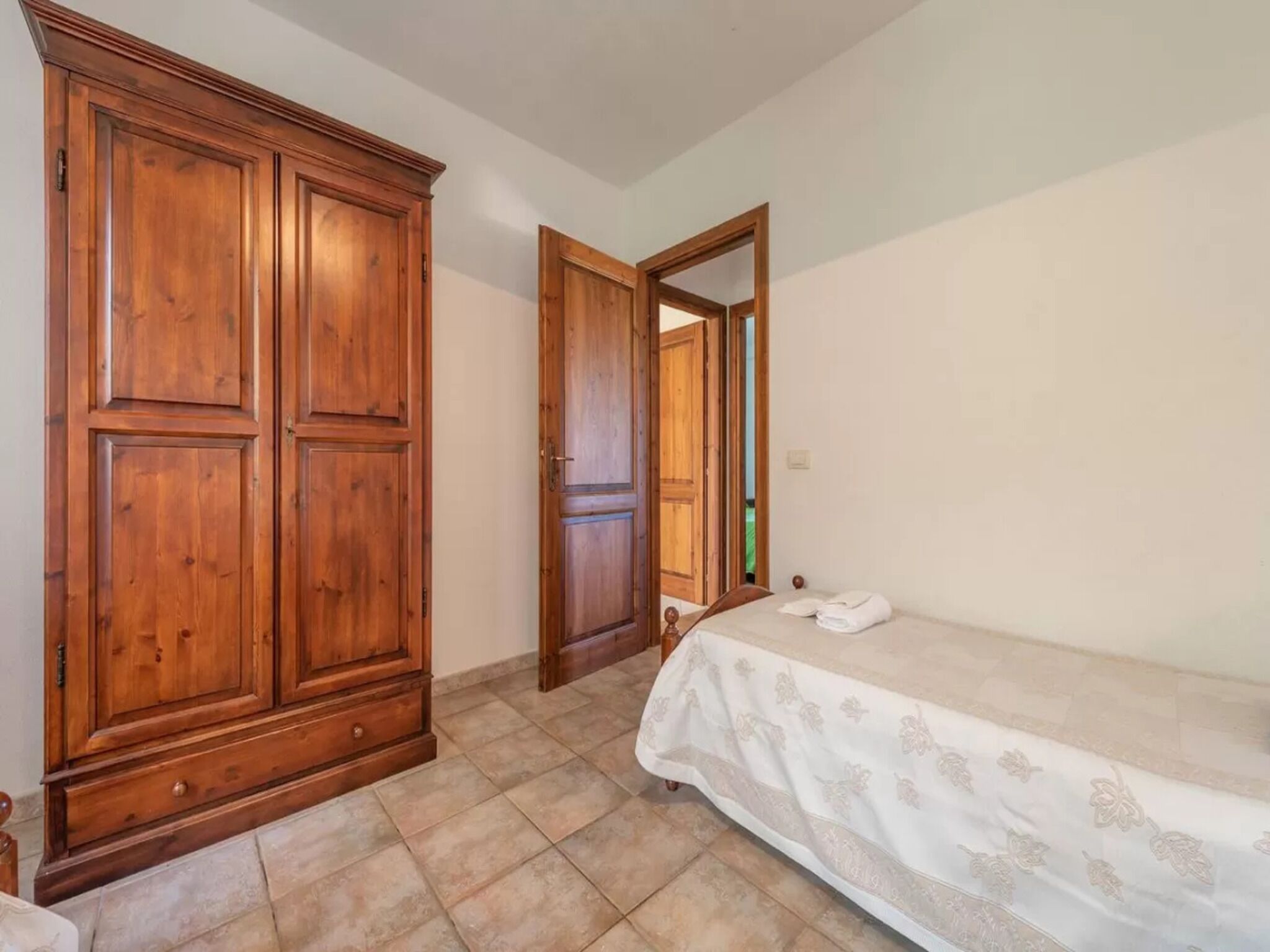 A room with a bed, a wooden wardrobe, and a door leading to another room.