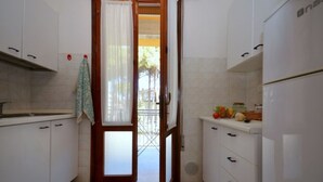 A narrow kitchen with white cabinets, a tiled backsplash, and a door leading to an outdoor area. - Modern flat for groups in Bibione (Bibione Pineda)
