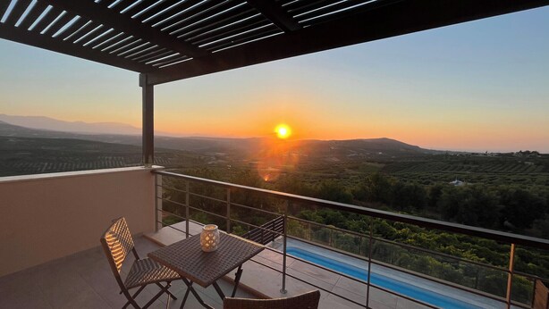 Ein Balkon mit Tisch und Stühlen mit Blick auf einen Swimmingpool und eine reizvolle Landschaft bei Sonnenuntergang.