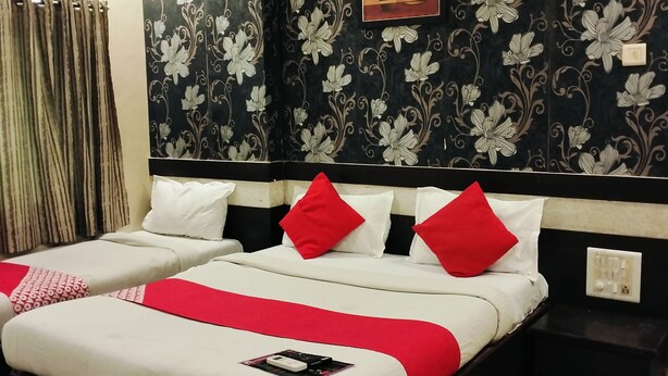 A hotel room with a large bed, two bedside tables, a wall clock, and a power outlet. - Hotel Palkhi (Rahata)