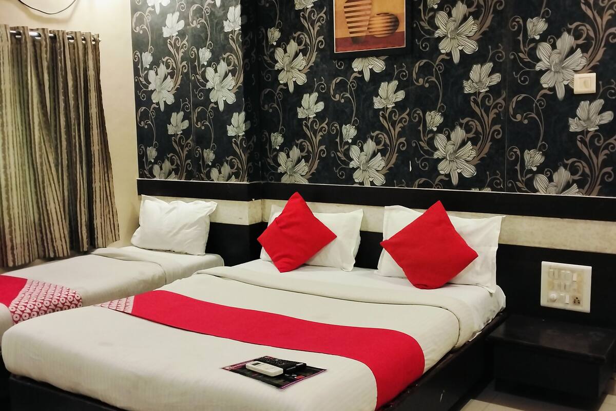 Una habitación de hotel con una cama grande, dos mesitas de noche, un reloj de pared y un enchufe.