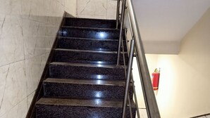 A staircase with dark marble steps and metal handrails, leading to a landing with a red fire extinguisher. - Hotel Palkhi (Rahata)