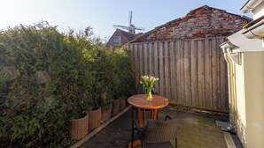 Une terrasse avec une table ronde en bois et deux chaises, une clôture en bois et un moulin à vent en arrière-plan.
