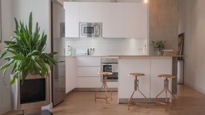 A modern kitchen with white cabinets, stainless steel appliances, and a central island with stools. - Urban Spring (Madrid)