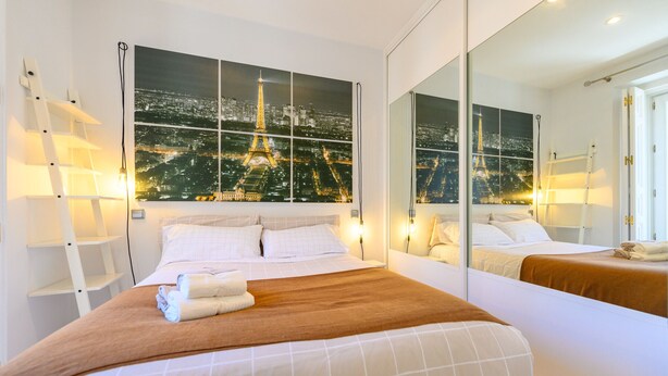 Une chambre d’hôtel avec un grand lit, une vue nocturne sur la Tour Eiffel et un miroir qui reflète le lit et la fenêtre.