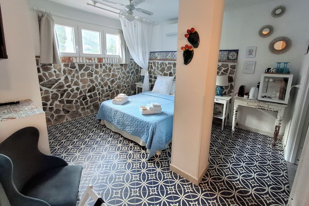 Ein Schlafzimmer mit einem Bett, einem Schreibtisch, einem Stuhl, einem Deckenventilator und einer Steinwand.