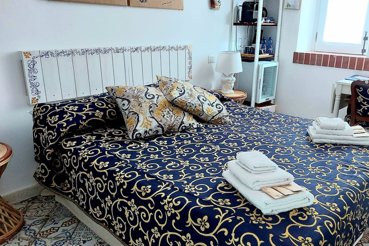 Ein ordentlich bezogenes Bett mit einer blauen und goldenen Bettdecke, einem hölzernen Kopfteil und einem Nachttisch mit Lampe und einer kleinen Statue.