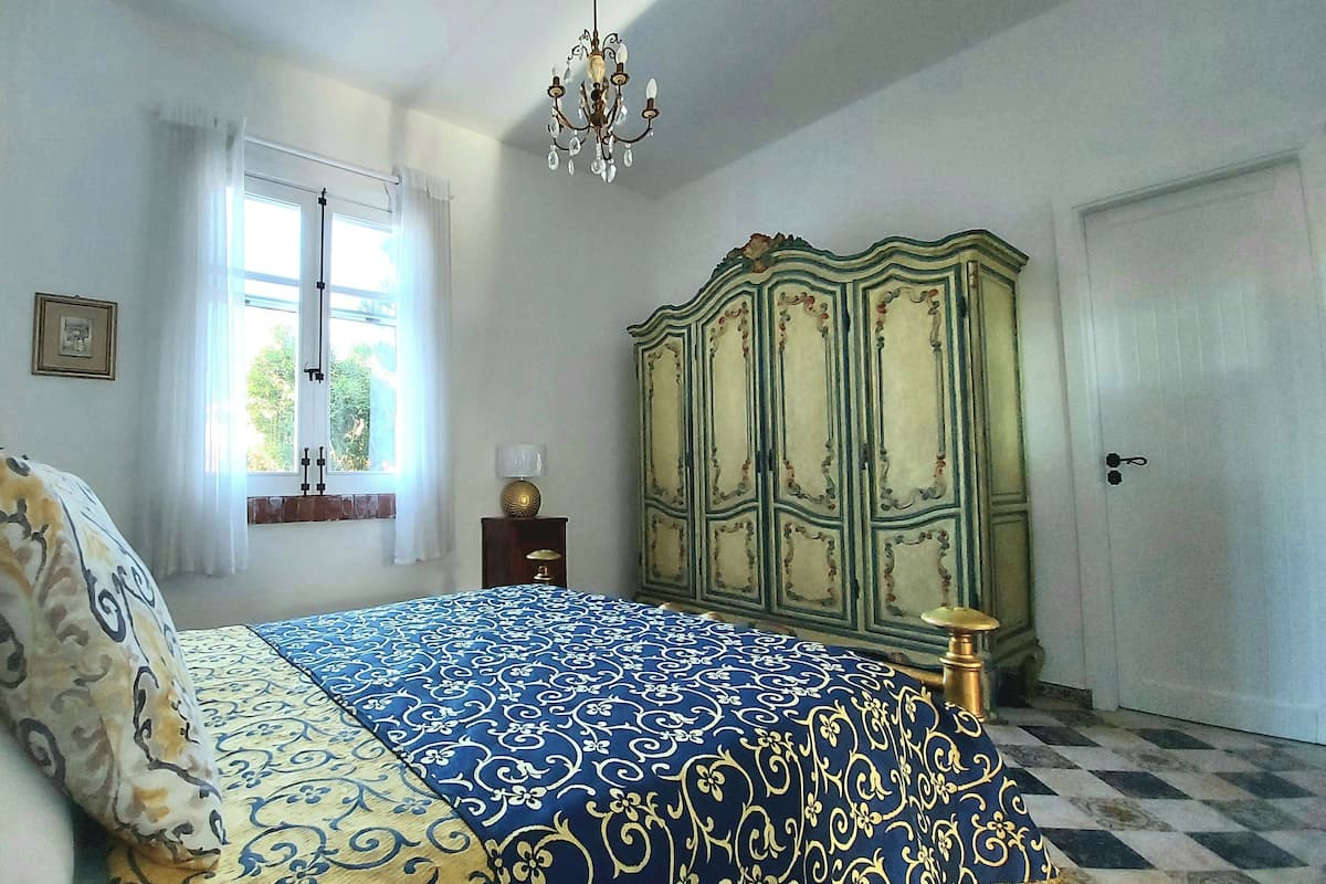 Ein Schlafzimmer mit Bett, Kleiderschrank, einer Deckenleuchte und einem Fenster mit Vorhängen.