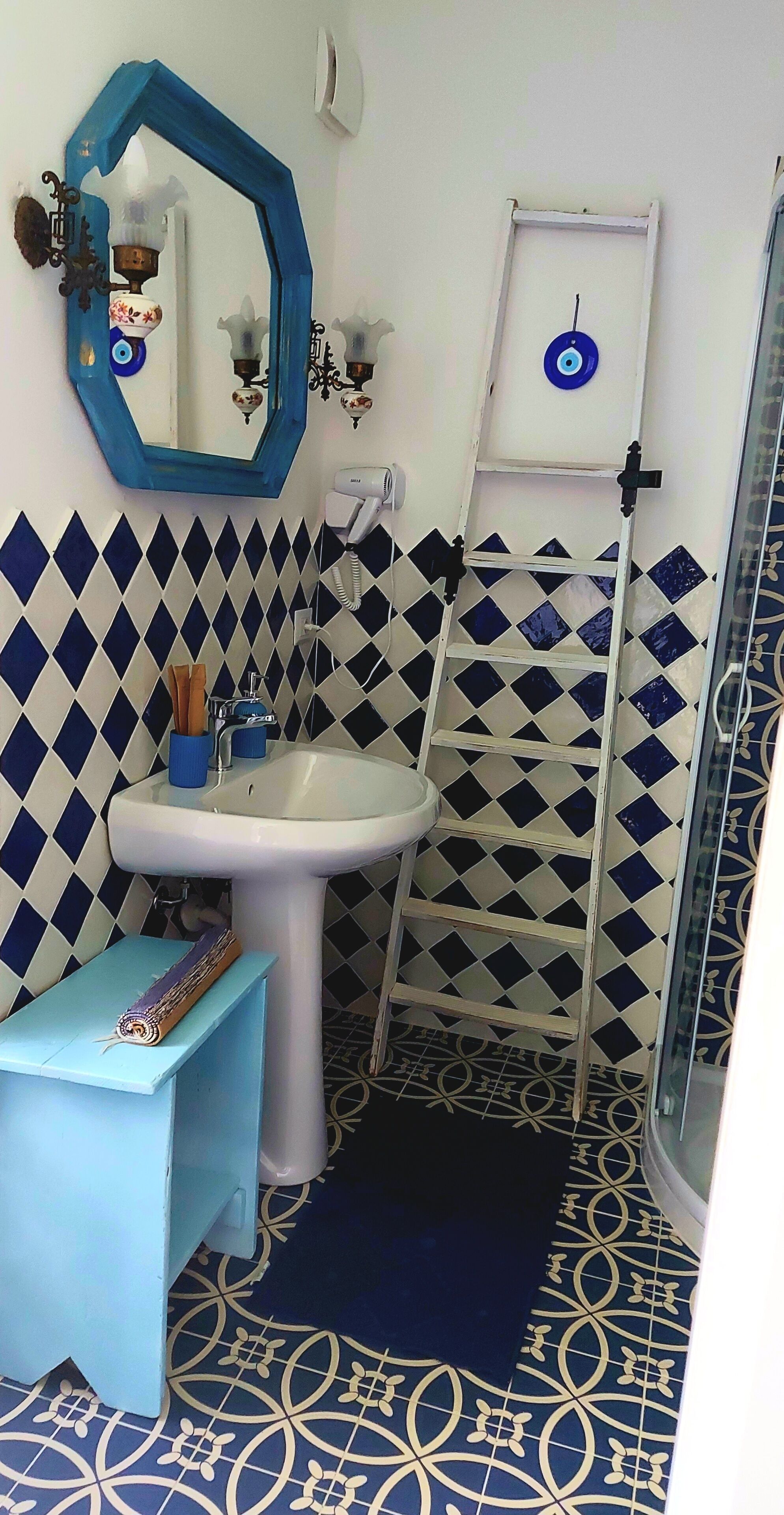 Un bagno con un lavandino bianco, piastrelle azzurre e bianche, uno specchio blu e un tappetino azzurro.