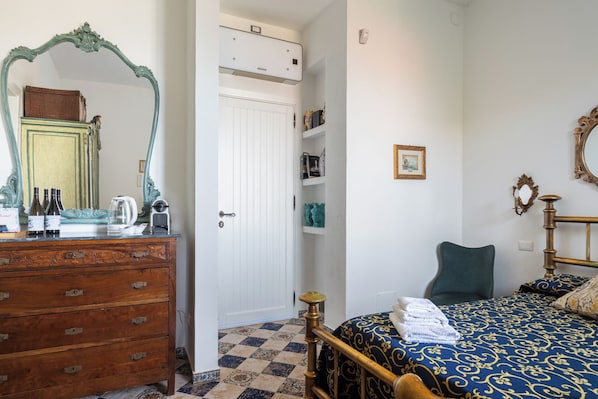 A bedroom with a wooden dresser, a bed with a blue and gold patterned bedspread, a green chair, and a white door with a radiator above it. - VFH Villa Flavia Eco B&B (Santa Flavia)