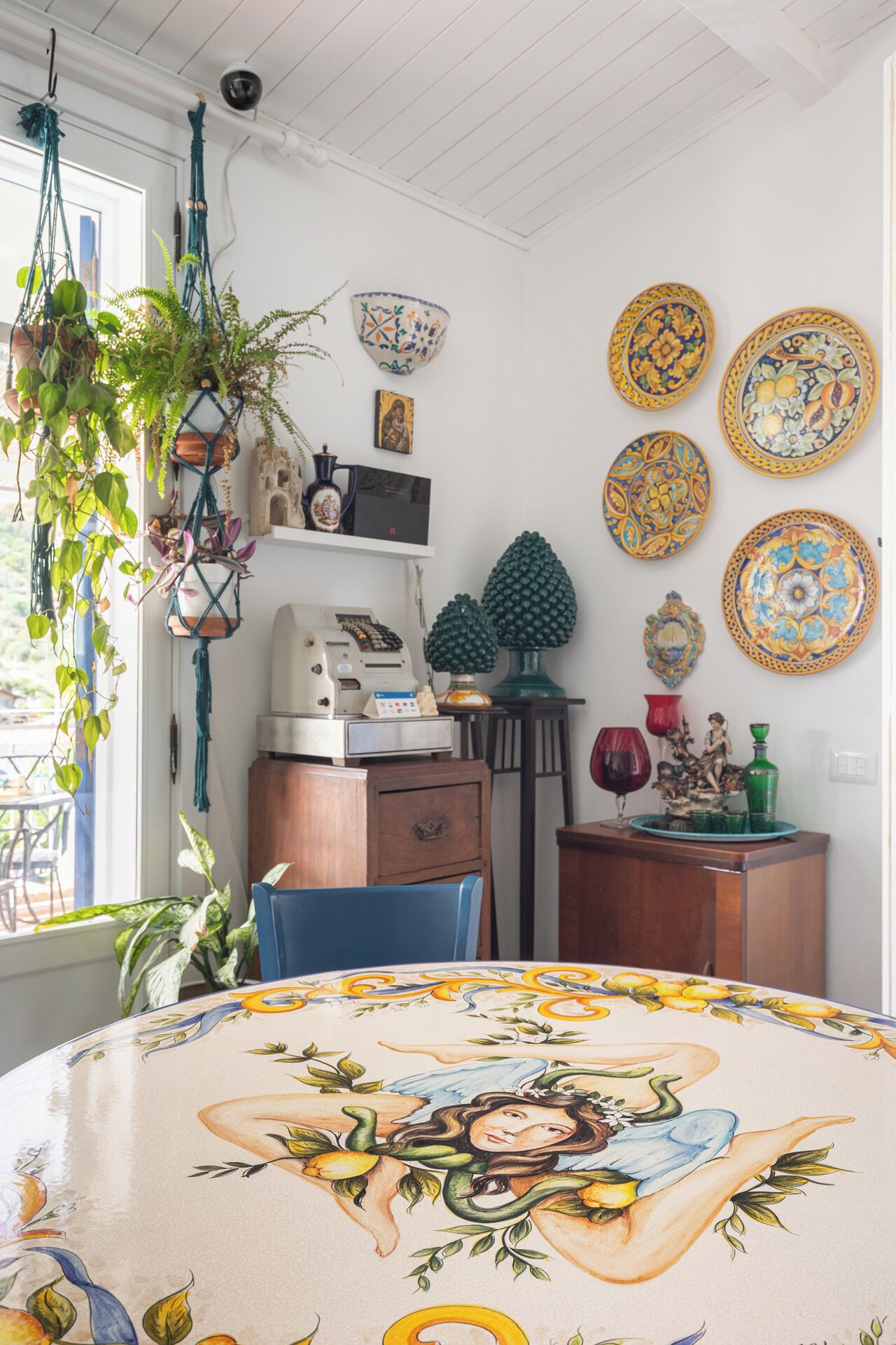 Een kamer met een ronde tafel, versierd met een bloemendecor, een koffieapparaat, een klein beeldje en verschillende decoratieve borden aan de muur.