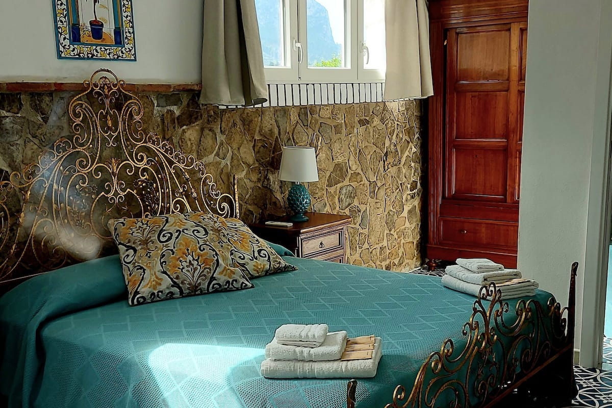 Ein Schlafzimmer mit einem Bett, einem Nachttisch, einer Lampe, einem Fenster mit Vorhängen, einer Wanddekoration und einem hölzernen Kleiderschrank.