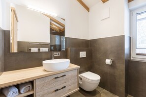 Ein modernes Badezimmer mit einem Holzwaschtisch, einem großen Spiegel, einem weißen Waschbecken, einer Toilette und einem Duschbereich.