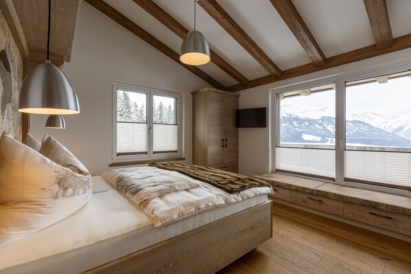 Un dormitorio con una cama grande, vigas de madera, un televisor y vistas a montañas.