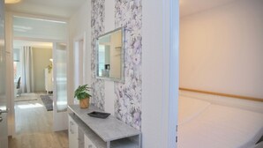 A modern bedroom with a bed, a bedside table with a plant, a mirror, and a bathroom visible in the background. - Relaxing vacation in the Panorama Whg. 8 - near the beach and the sea! (Grömitz)