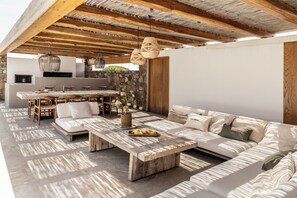 Un espacio exterior con techo de madera, pared de piedra, cocina integrada y un sofá grande.