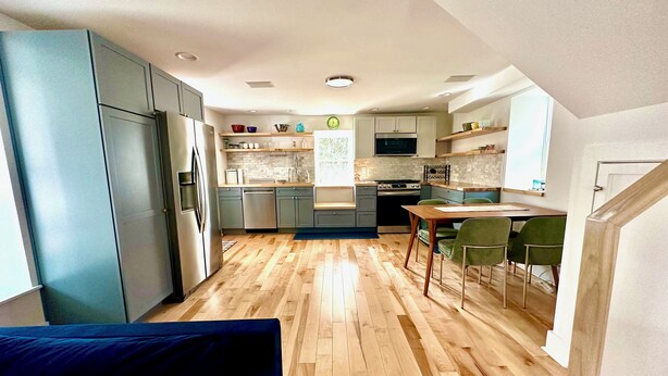 A modern kitchen with grey cabinets, a wooden floor, and a dining area with green chairs. - Charming 1-bedroom cottage on Wissahickon Park in Chestnut Hill (Philadelphia)
