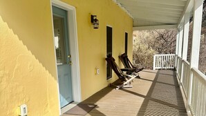A covered porch with a yellow wall, a door, and two wooden chairs. - Charming 1-bedroom cottage on Wissahickon Park in Chestnut Hill (Philadelphia)