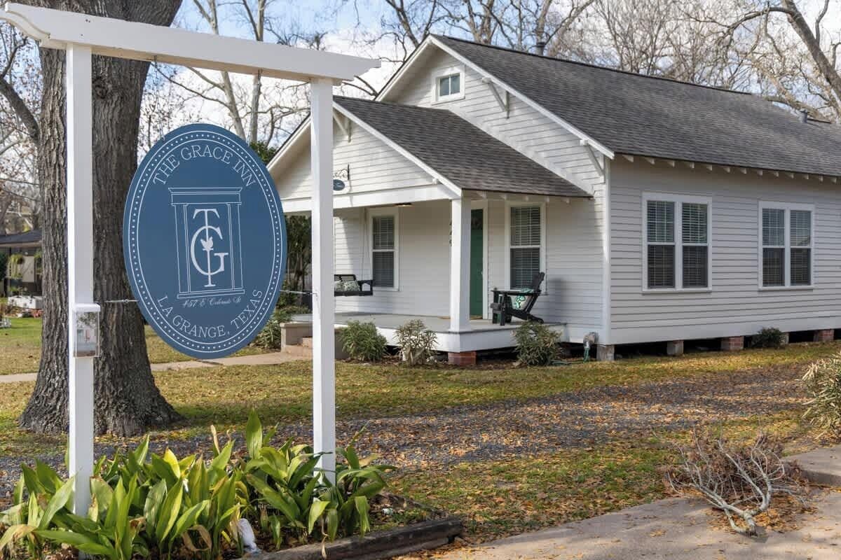 A white house with a porch, a sign for The Grace Inn, and a tree in the foreground.