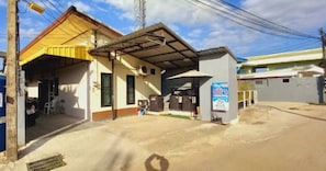 A building with a covered entrance, a small outdoor seating area, and a signboard.
