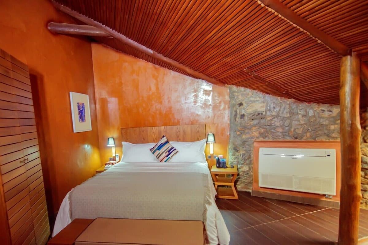A bedroom with a bed, bedside lamps, a telephone, and a wall-mounted air conditioner.