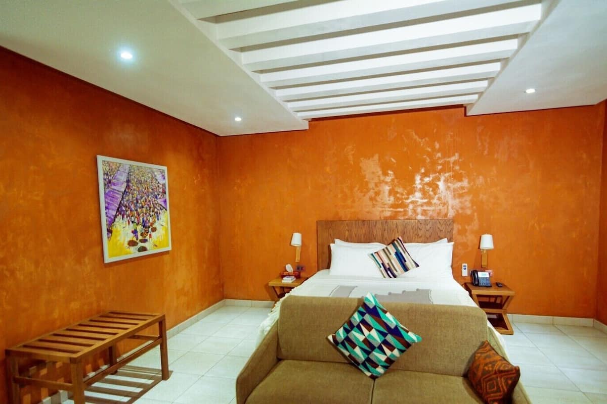A hotel room with a large bed, two bedside tables, a wooden bench, and an orange wall.