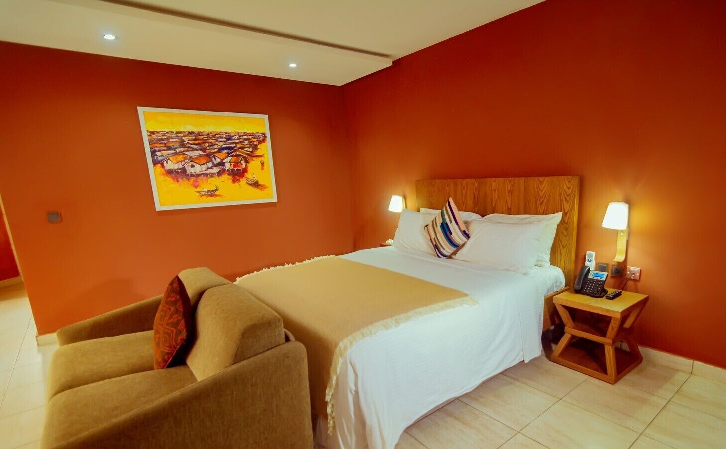 A hotel room with a large bed, two bedside tables with lamps, a chair, and a painting on the wall.