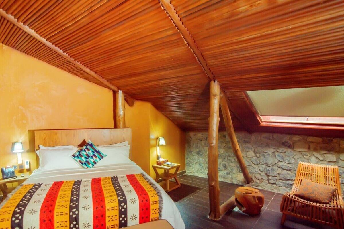 A cozy room with a sloped ceiling, a bed with a colorful blanket, a stone wall, and a wooden chair.