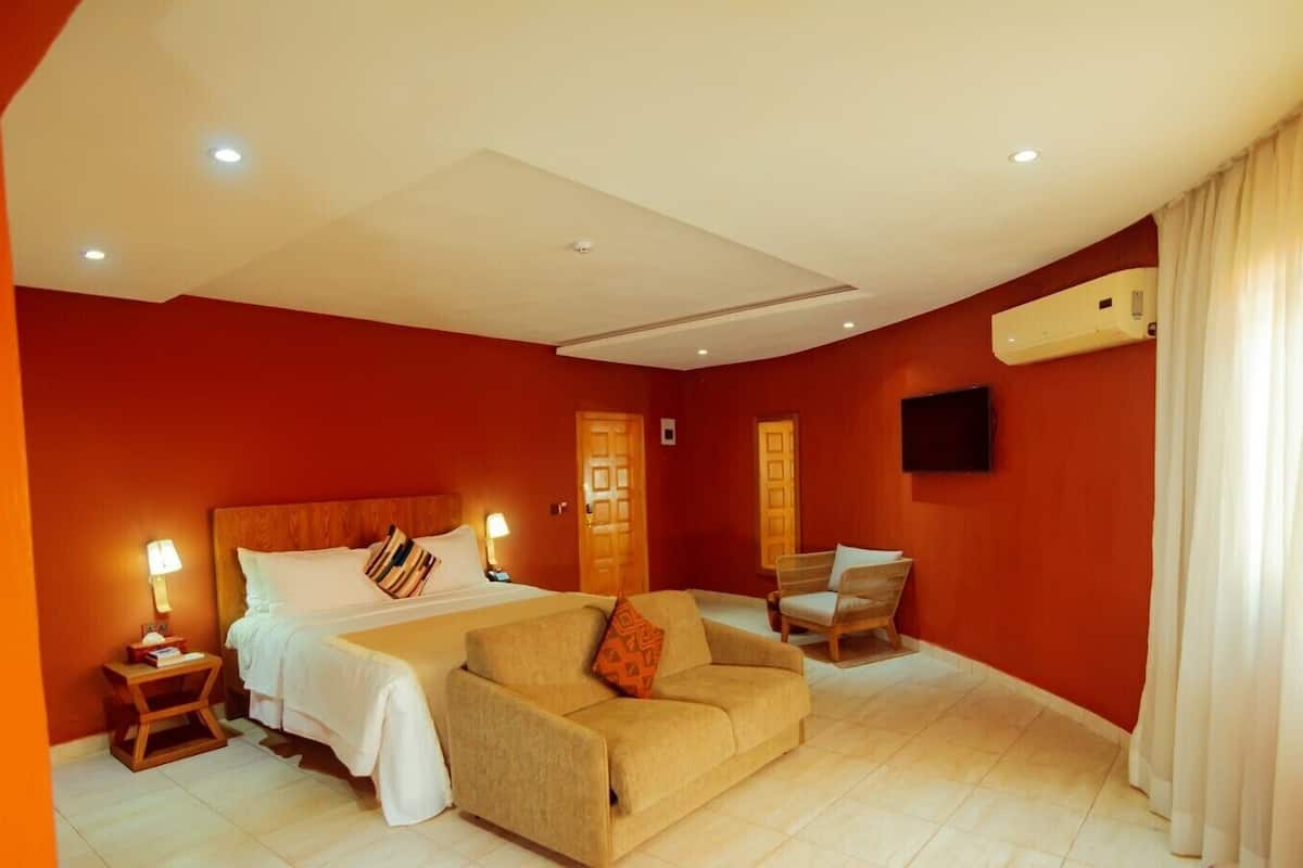 A hotel room with a bed, a sofa, a chair, and a TV on the wall.