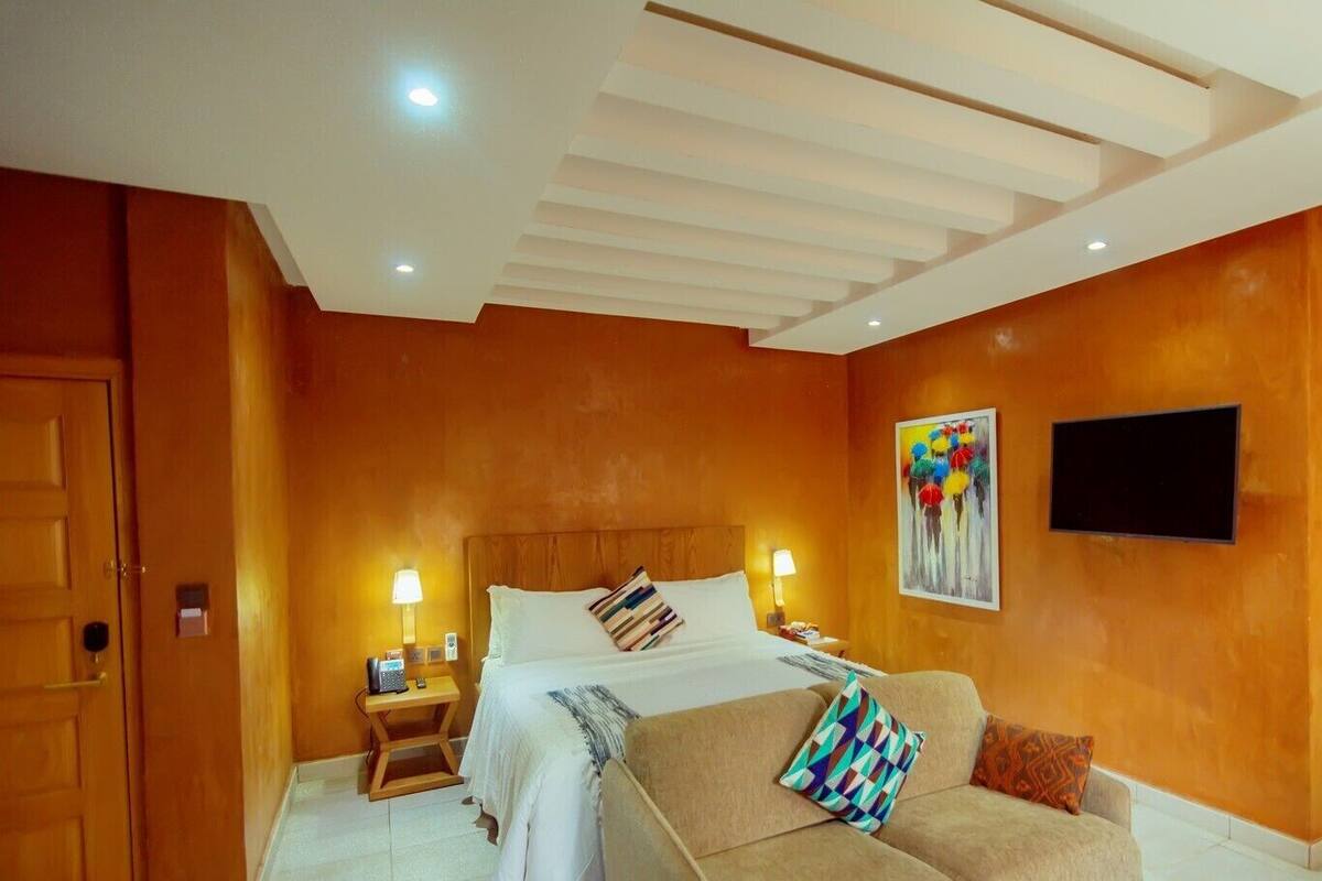A hotel room with a bed, a sofa, a TV, and wooden walls.