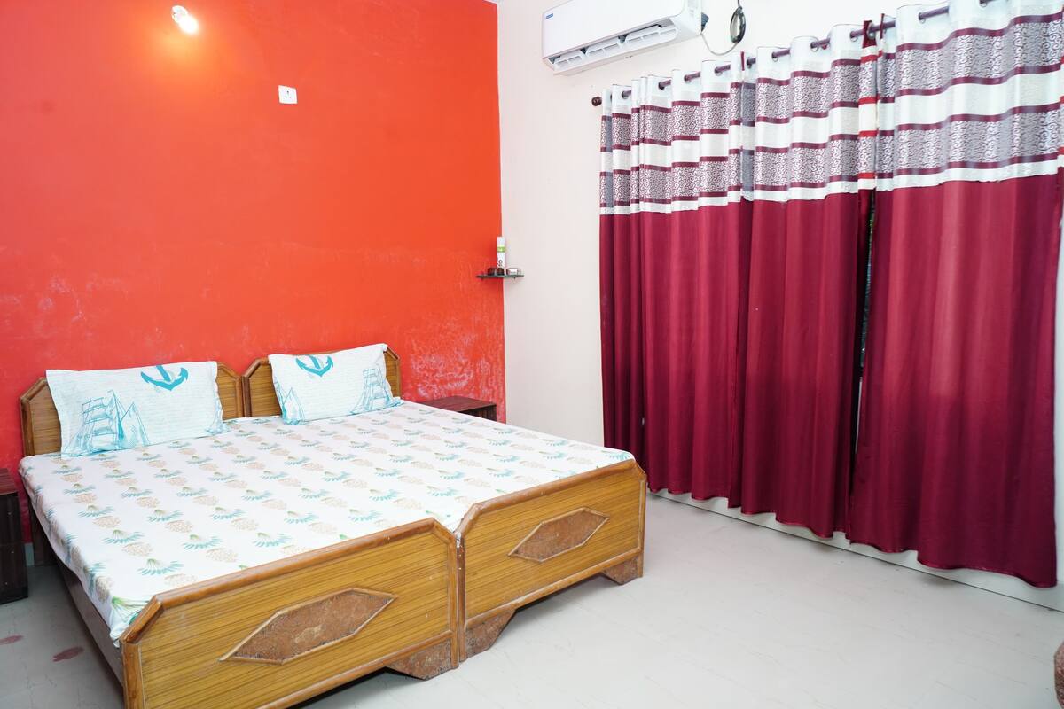 A room with a bed, a red wall, and a window with red curtains.