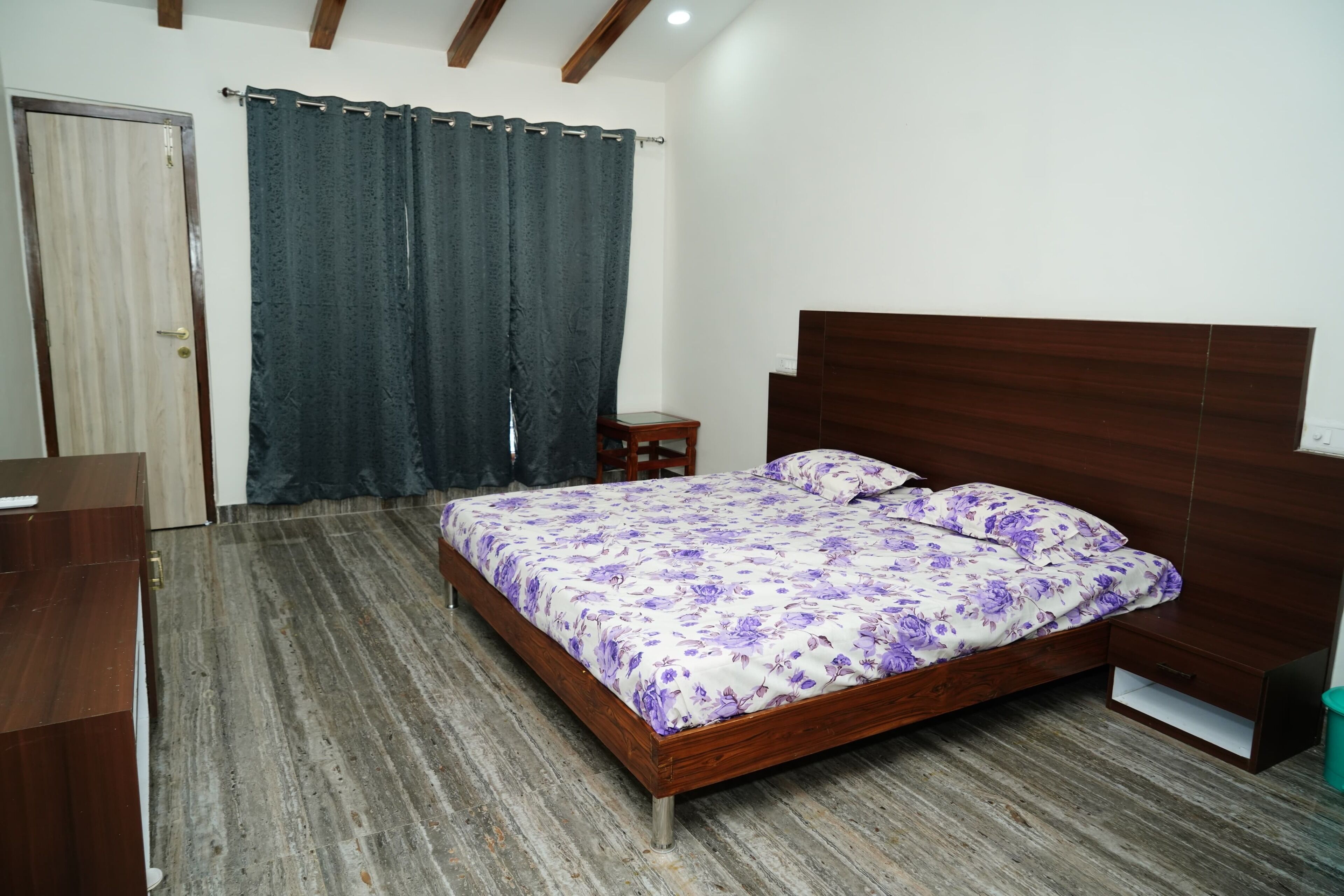 A bedroom with a wooden bed, a nightstand, a wooden wardrobe, and a dark curtain.