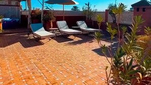 Une terrasse sur le toit avec un sol carrelé, deux chaises longues et des plantes en pot.