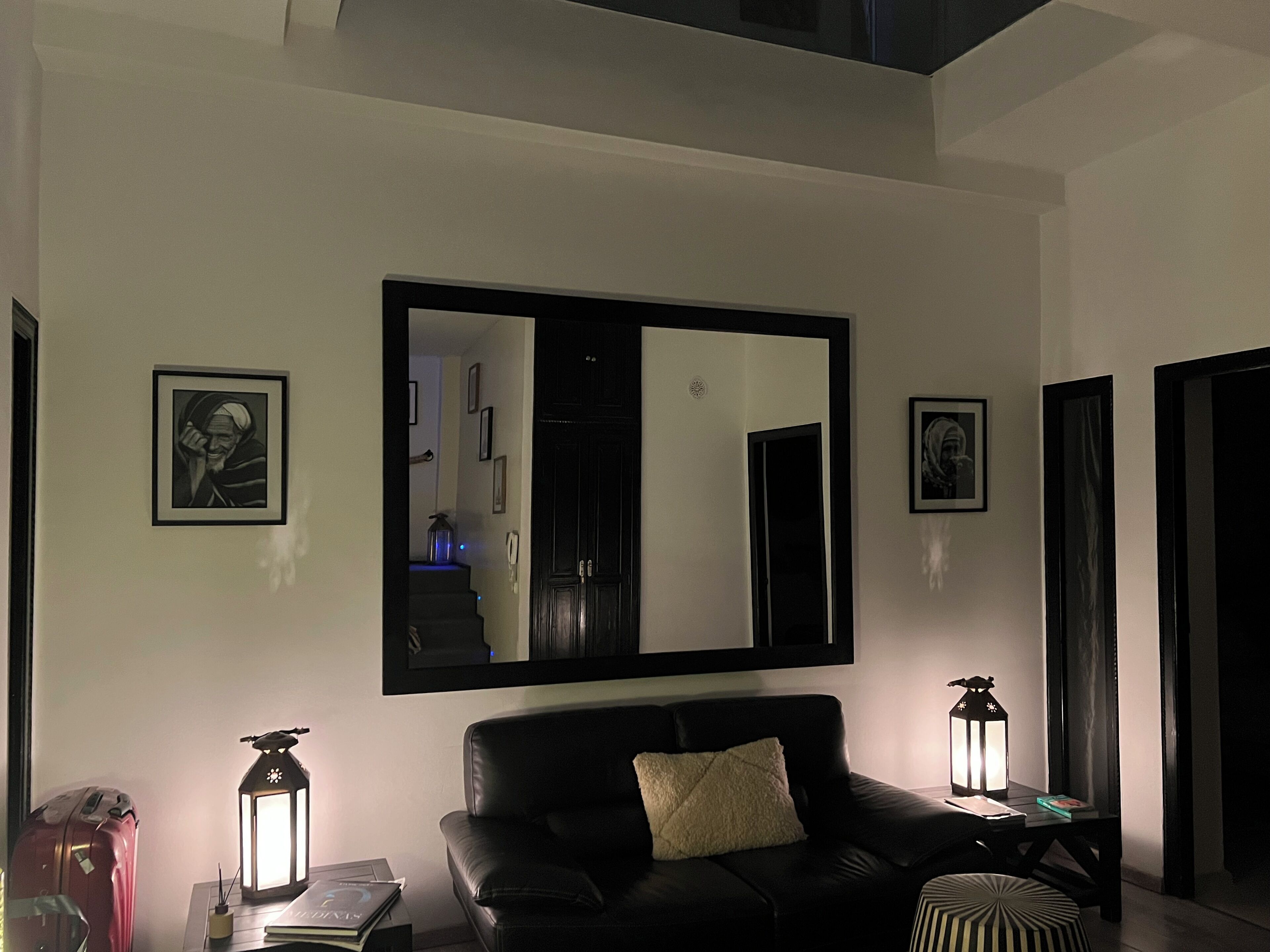 A modern living room with a black leather sofa, a large mirror, and two wall-mounted lanterns.