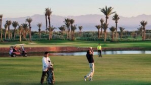 Un parcours de golf avec un ciel dégagé, des palmiers et une chaîne de montagnes à l’horizon.