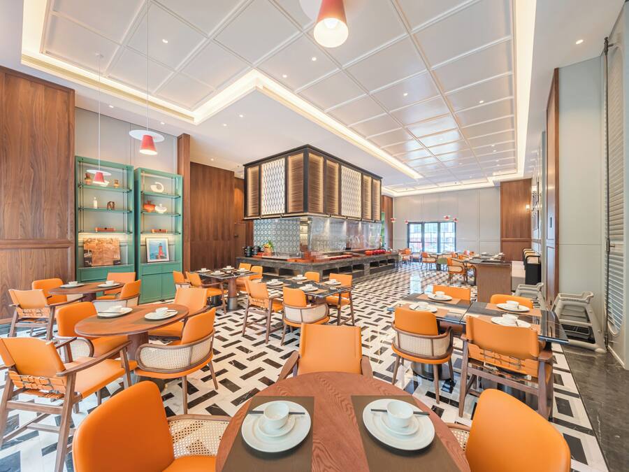 A modern dining area with round tables and orange chairs, a bar area, and a patterned floor.