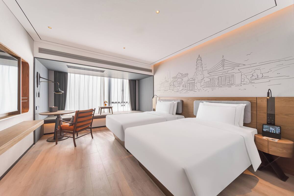 A hotel room with two beds, a desk, a chair, and a wall mural.