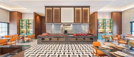 A spacious hotel lobby with a central seating area, multiple dining tables, and green bookcases.