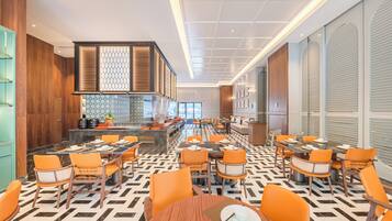 A modern restaurant with a geometric patterned floor, orange chairs, and a central bar area.