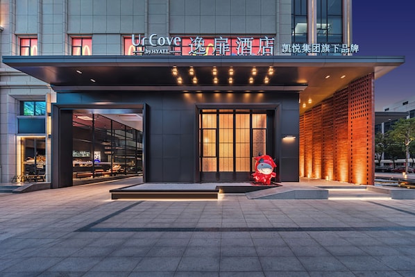 A modern hotel entrance with a large glass facade, a red mascot sculpture, and illuminated signage. - UrCove by Hyatt Shantou Xinyicheng Huanghe Road (Shantou)