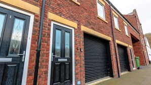 A row of brick buildings with black garage doors, a green trash bin, and a visible number '2' on the door. - Beach Stay on the North Yorkshire Coast (Skinningrove)