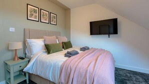 A bedroom with a bed, a nightstand, a lamp, a TV mounted on the wall, and framed pictures on the wall. - Beach Stay on the North Yorkshire Coast (Skinningrove)