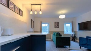 A modern kitchen with a white countertop, a built-in oven, and a black island. There are three pendant lights above the counter and a large window with curtains. - Beach Stay on the North Yorkshire Coast (Skinningrove)