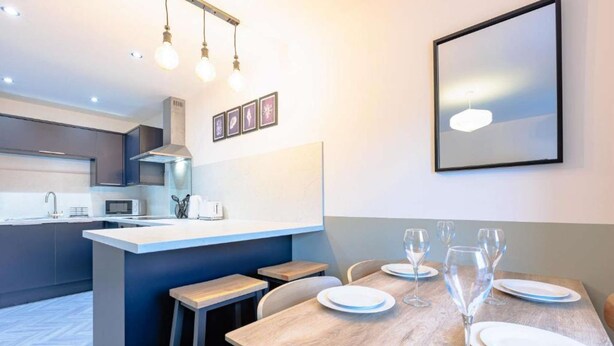 A modern kitchen with a central island, bar stools, and a dining area with a table set for six. - Beach Stay on the North Yorkshire Coast (Skinningrove)