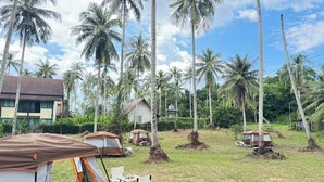 A campsite with tents and palm trees, surrounded by a grassy area and a building in the background. - Tent Room Koh Kood (Ko Kut)