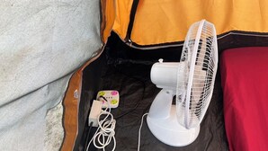 A white fan with a power strip plugged in, a small decorative item, and a red blanket on a black and orange tent. - Tent Room Koh Kood (Ko Kut)
