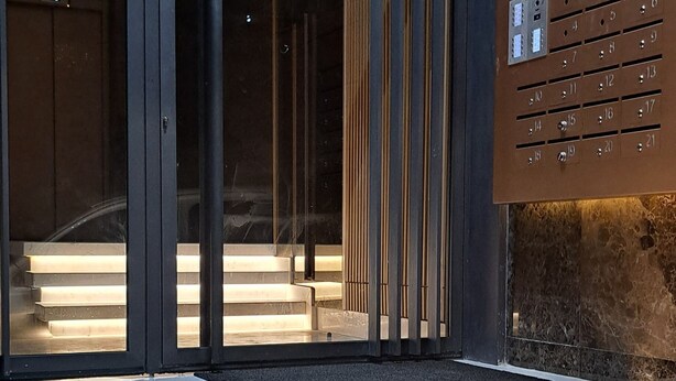 A modern building entrance with a glass door, a wooden bench, and a metal elevator with numbered buttons. - Cozy Elegant Apartment - Rabat Center- Free Parking & AirC & Internet (Rabat)