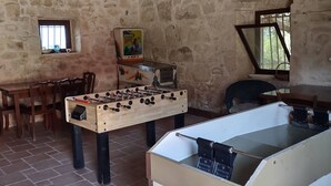 A rustic room with a foosball table, a wooden table, and chairs.